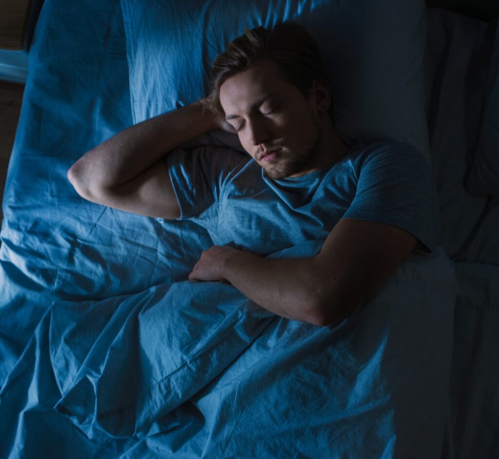Top view of young man sleeping on bed at night