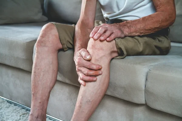 A person sitting on a couch, holding their knee, possibly indicating discomfort or venous disease.