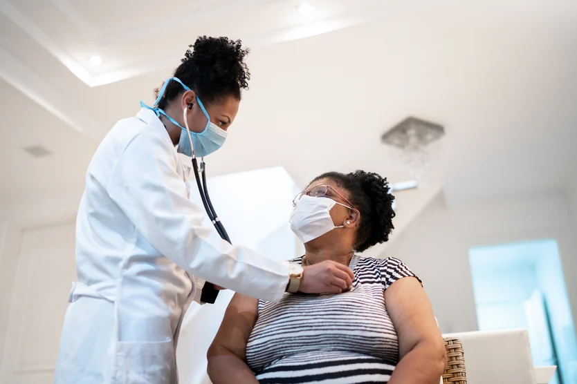 A healthcare professional in a white coat and mask is administering a vaccine to a patient, who is seated and also wearing a mask, in the cardiology department.