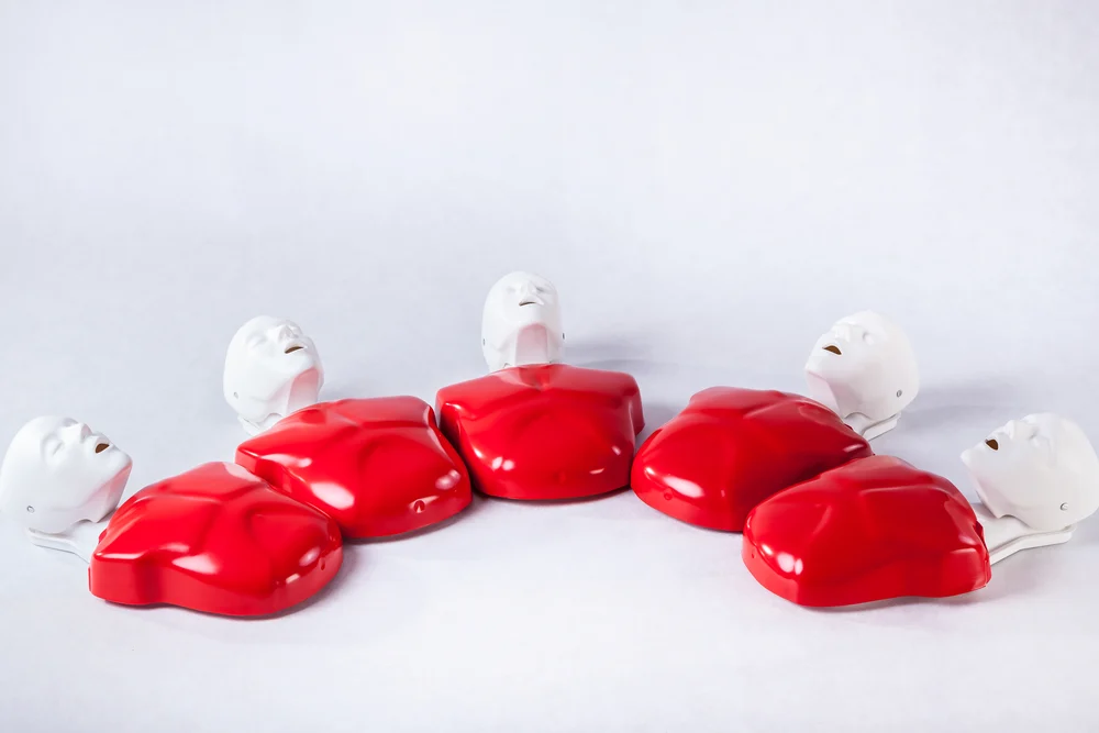 A row of red and white CPR training manikin heads and torsos, arranged by the Cardiovascular Institute of the South on a light background for heart health education.