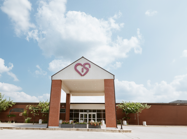 Modern brick building with a unique heart-shaped logo on the facade under a blue sky with fluffy clouds.