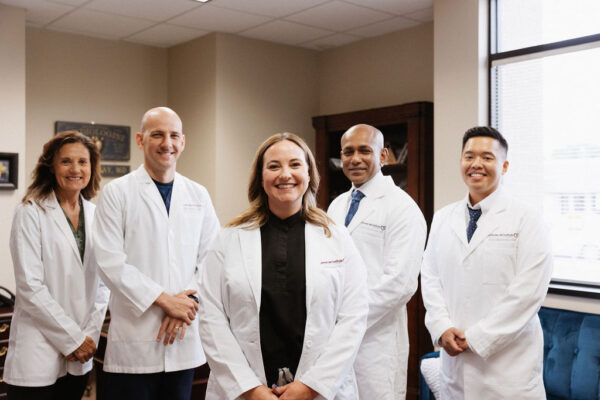A team of confident cardiologists smiling in their white lab coats, standing together in a medical office setting.