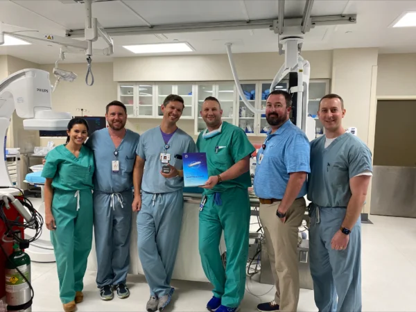 A group of CIS staff poses with a box containing the Abbott Assert IQ ICM in an operating room