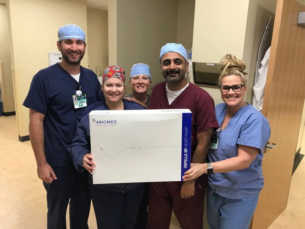 A group of CIS staff members pose next to a box containing an Impella device