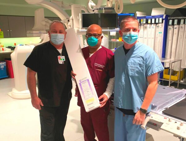 A group of CIS staff members in scrubs pose with a box containing the Sentry Bioconvertible Inferior Vena Cava (IVC) Filter