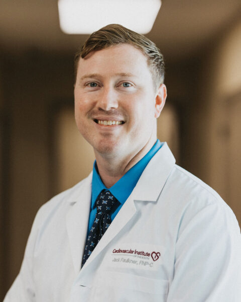 A professional portrait of a smiling cardiologist wearing a white lab coat with a name tag and possibly a logo of the Cardiovascular Institute of the South embroidered on it, signifying his affiliation to a healthcare