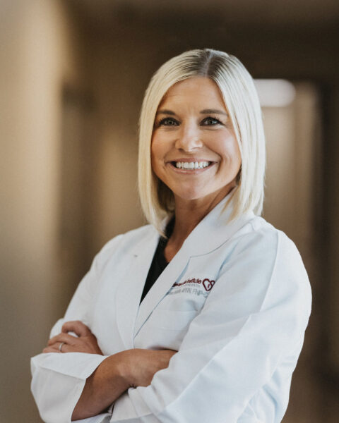 A confident cardiologist in a white lab coat smiling warmly, with her arms crossed.