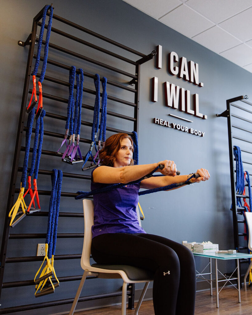 A cardiac rehab fitness instructor helps to demonstrate proper seated technique for using resistance bands