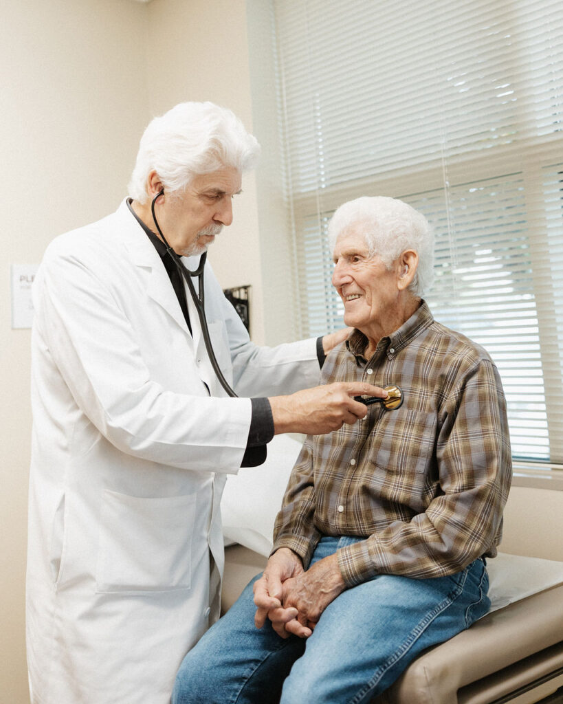 A senior man with a smile being examined by a doctor using a stethoscope during a medical check-up.