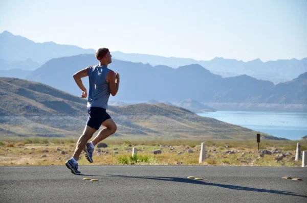 A runner in athletic attire enjoying a jog on a sunny day with a picturesque backdrop of mountains and a serene lake, enhancing their heart health.