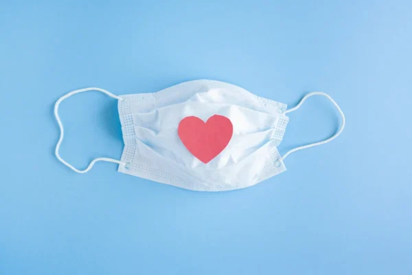 A surgical mask with a red heart on it, placed against a blue background, symbolizing cardiologist's care and love in the time of health crises.