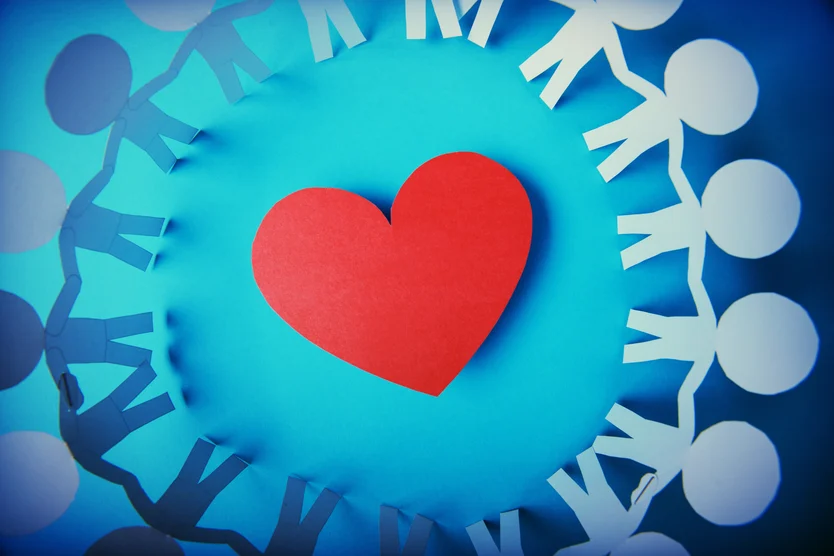 Circle of paper people holding hands around a red heart on a blue background, symbolizing unity and love in cardiology.