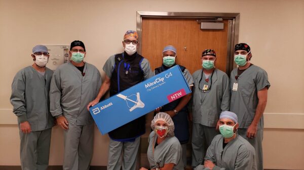 A group of CIs staff members in scrubs posing with a box containing the MitraClip G4 Clip Delivery System