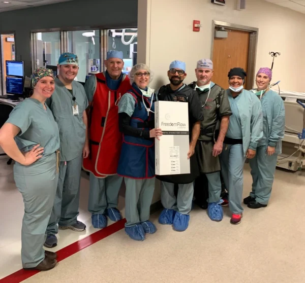 A smiling group of CIS staff in scrubs poses with a box containing the Freedom Flow system