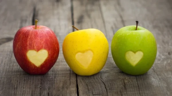 Three colorful apples with heart-shaped cutouts on a wooden surface representing cardiology.