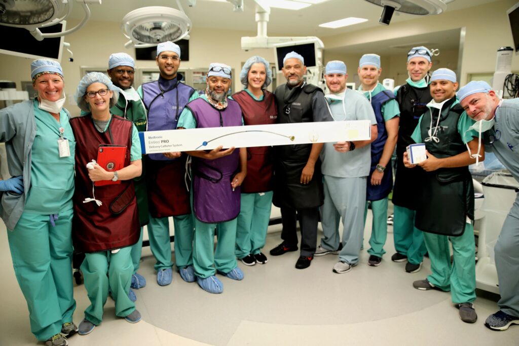A group of smiling CIs staff members pose with a box containing the EnVeo Pro Delivery Catheter System
