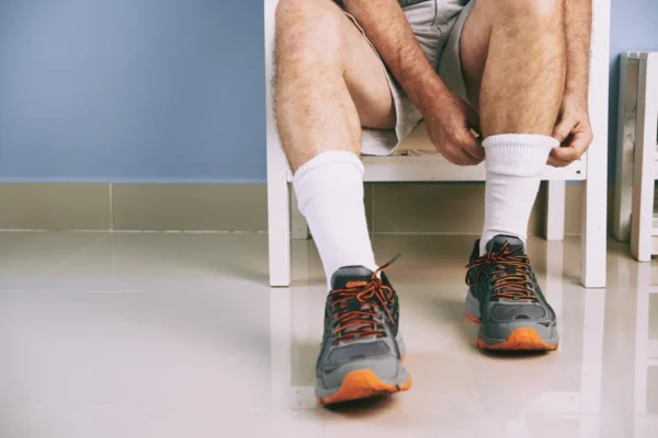 A person sitting on a bench in a locker room, wearing sports shoes and white socks, preparing for physical activity or rest after exercising, mindful of their heart health.