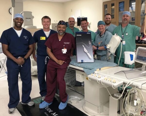 A smiling group of CIs staff members poses with a ROTAPRO device in an operating room