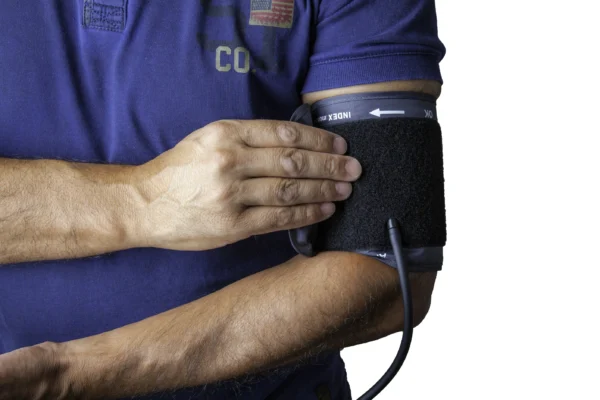 A person self-administering a blood pressure test using a sphygmomanometer cuff on their upper arm to monitor heart health.