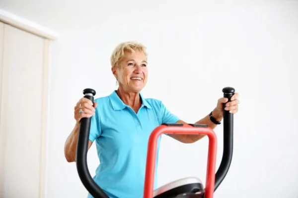 Senior woman with a joyful smile exercising on an elliptical trainer to improve her heart health under the guidance of a cardiology team.