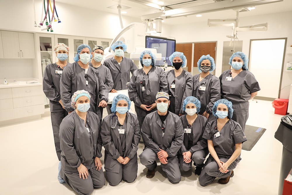 A group of CIS staff members in matching gray scrubs poses for a photo in an operating room
