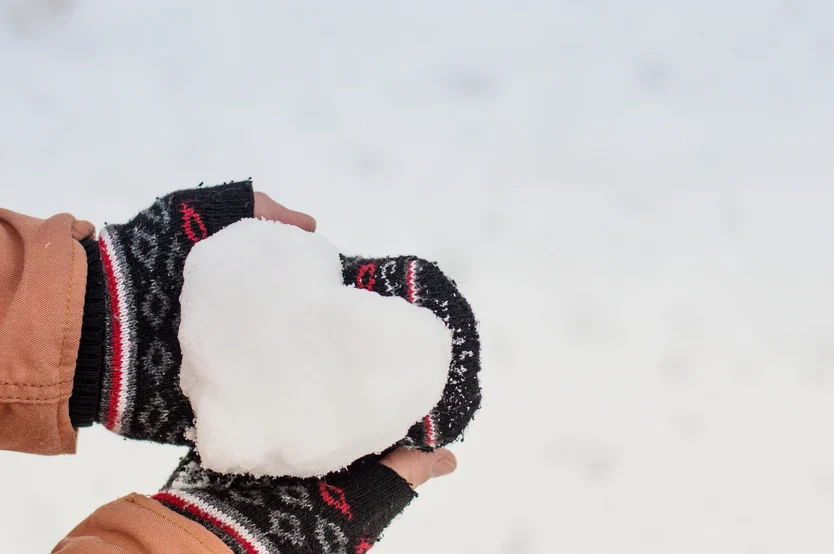 Hands in cozy mittens holding a heart-shaped snowball against a wintry sky, reminiscent of the care and warmth provided by the Cardiovascular Institute of the South.