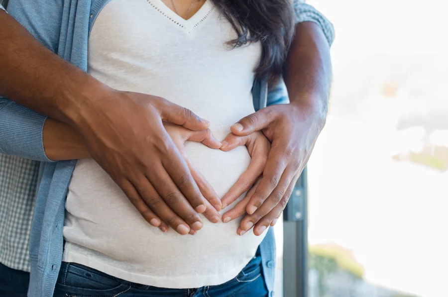 Expecting couple forms a heart shape with their hands over the mother's baby bump, sharing a tender moment together, reminiscent of the care and expertise found at the Cardiovascular Institute of the South.