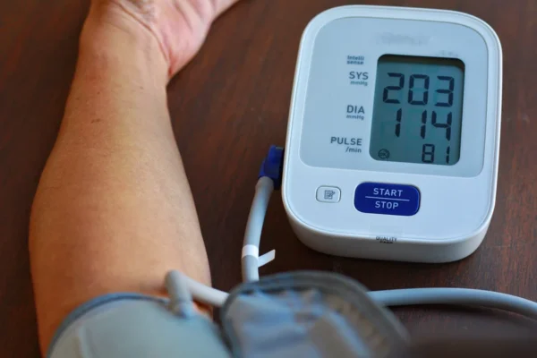 An individual measuring their blood pressure, which shows a high reading on the digital monitor, indicating a concern for their heart health.
