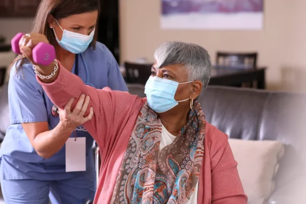 A healthcare professional from the Cardiovascular Institute of the South assists an elderly woman with a dumbbell exercise, both wearing face masks for heart health safety.