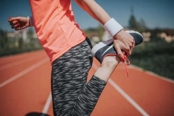 A runner on a track field stretching and tying her shoe, preparing for a workout or run to improve her heart health.