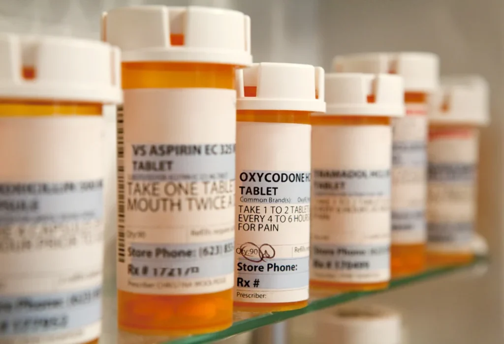 Row of prescription medication bottles on a shelf with focus on a bottle labeled "oxycodone," prescribed by a cardiologist.