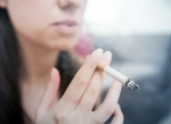 Close-up of a person holding a lit cigarette, with smoke drifting upward, evoking a moody and contemplative atmosphere, while subtly raising concerns about heart health.