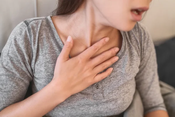 A woman experiencing discomfort, clutching her chest in a sign of pain or shortness of breath, may need to consult with a heart doctor.