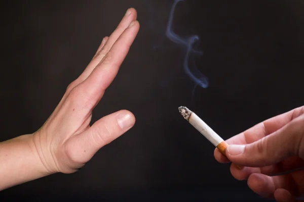 A person's hand gesturing "no" to an offered burning cigarette, symbolizing smoking refusal or quitting smoking, a vital measure endorsed by the Cardiovascular Institute of the South to combat venous disease