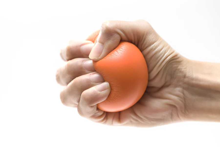 A hand tightly squeezing a red stress ball against a white background, symbolizing heart health maintenance advised by a cardiologist.