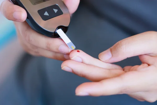 A person performs a blood glucose level test using a glucometer to manage diabetes and monitor heart health.
