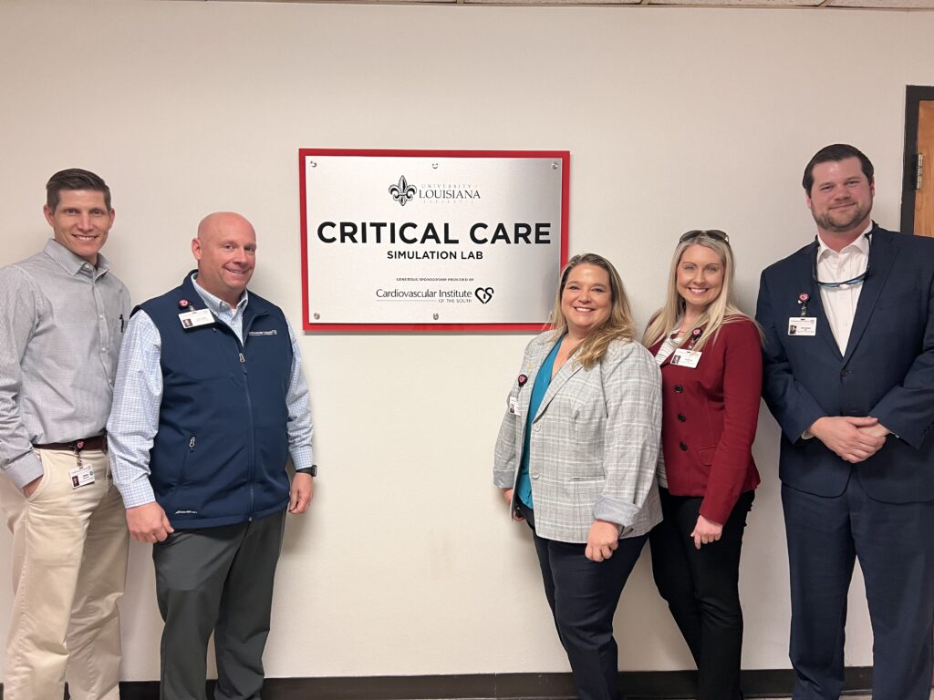 Group of healthcare professionals standing proudly in front of the "louisiana critical care simulation lab" sign.