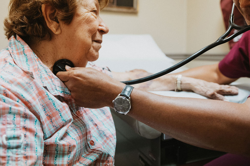 Elderly woman at wellness checkup, nurse holding stethescope to her neck