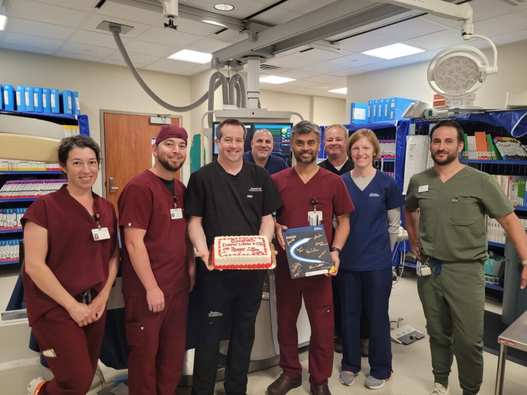 Eight medical professionals pose in a hospital room; two hold cakes with congratulatory messages, and everyone is smiling at the camera.
