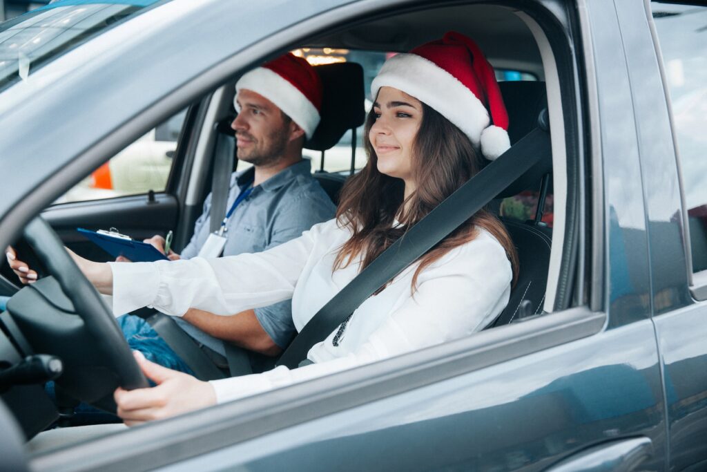 Two people sitting in the front seat of a car wearing Santa.
