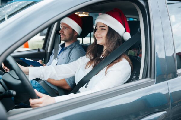Two people sitting in the front seat of a car wearing Santa.