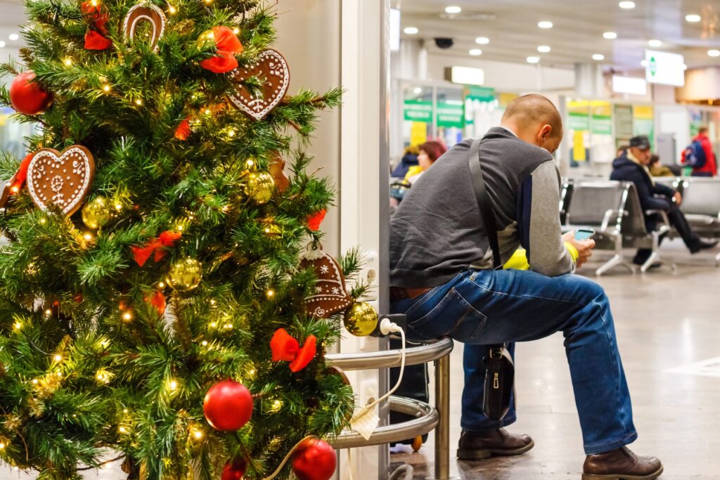Man waiting for flight at the airport, sitting near a Christmas tree