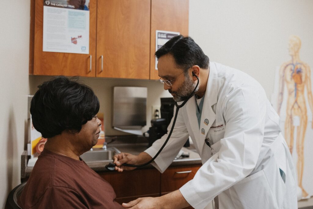 A doctor in a white coat uses a stethoscope to examine a patient seated in a medical office.
