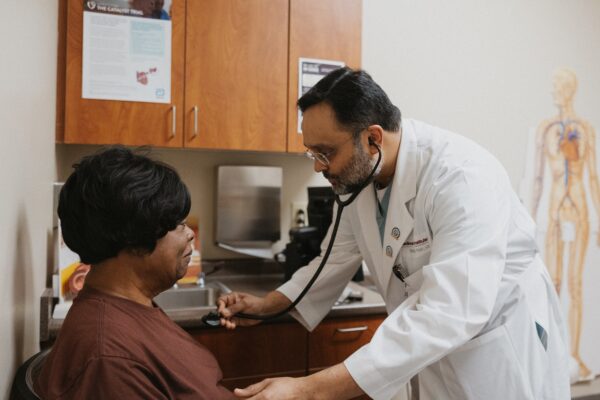 A doctor in a white coat uses a stethoscope to examine a patient seated in a medical office.