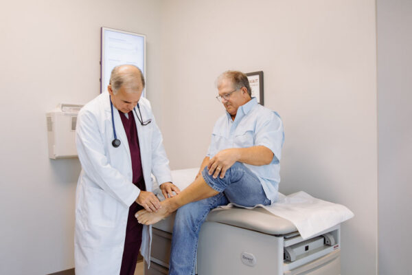 A doctor examines the ankle of a seated male patient.