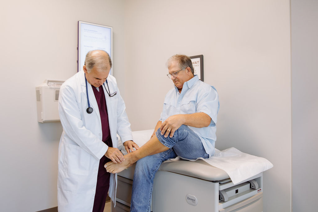 A doctor examines the ankle of a seated male patient.