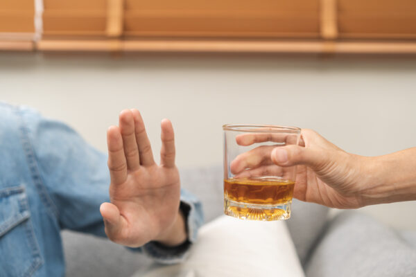 A person holds up their hand to refuse a glass of whiskey that another person is offering.