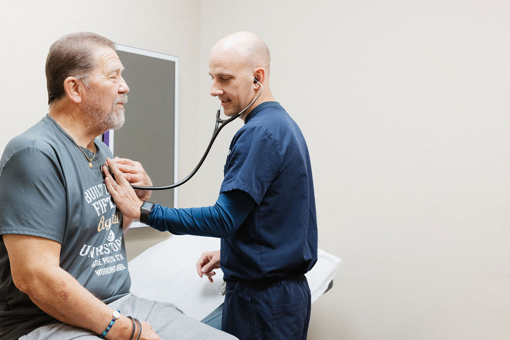 A healthcare professional uses a stethoscope to listen to a patient’s chest in a medical examination room.
