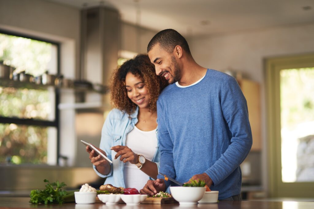 Happy young couple using a digital tablet while preparing a healthy meal together at home.