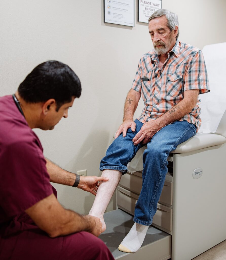 Nurse in red scrubs examining male patients calf in office